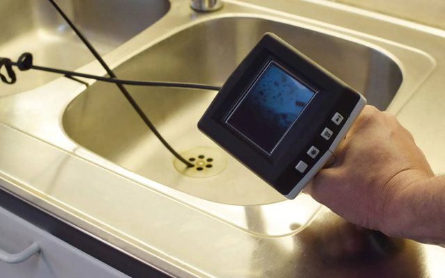 Handheld sewer camera inspection monitor displaying a live feed from inside a pipe