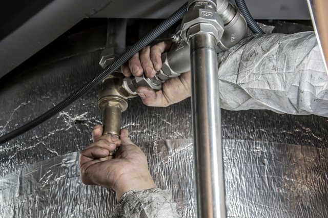 Close-up of hands working on pipe fittings under a sink