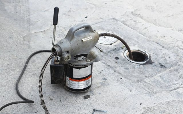 Electric drum auger machine clearing a drain line during a Tim's Pipes service call